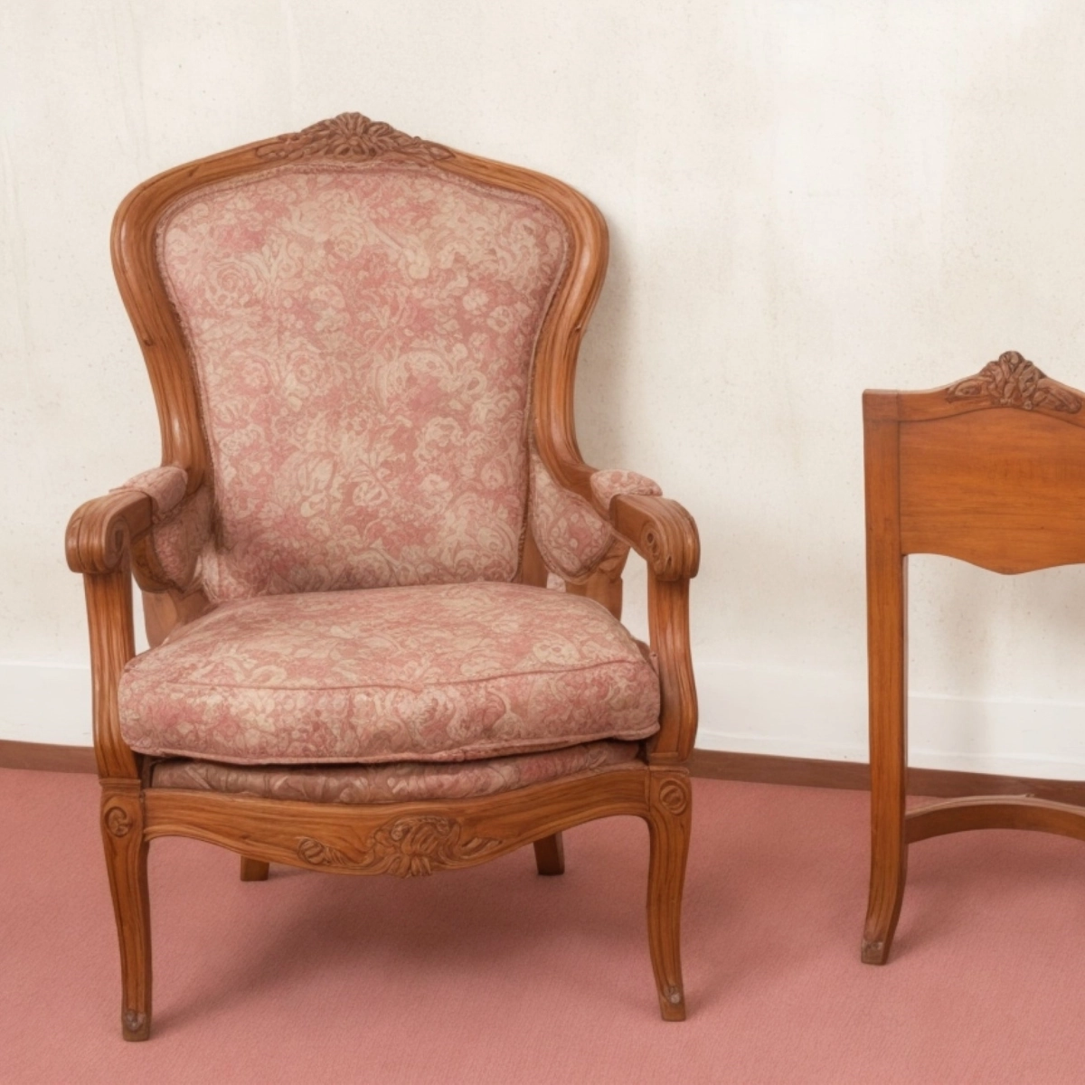Elegant vintage bergère chair with intricate woodwork and soft floral upholstery.