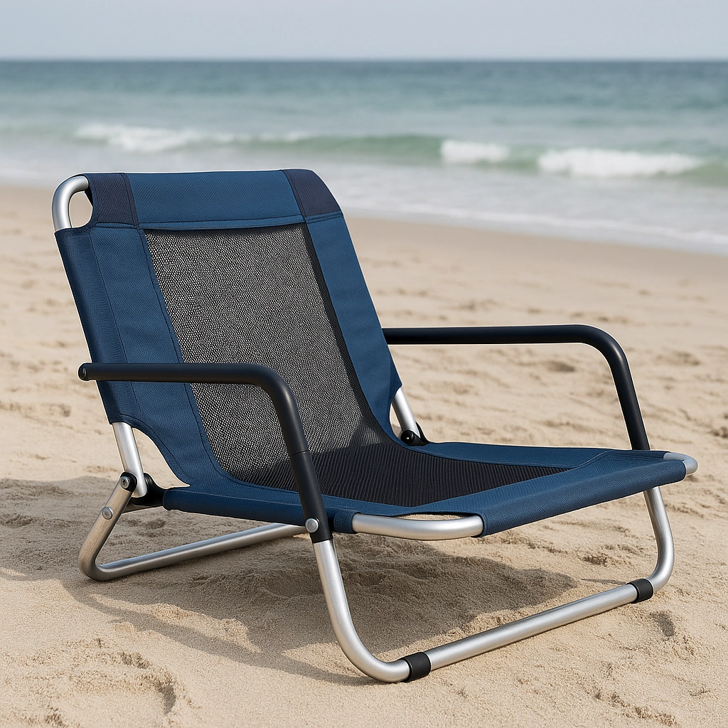 Low-profile beach chair with mesh backrest on sand, facing ocean waves under cloudy sky.