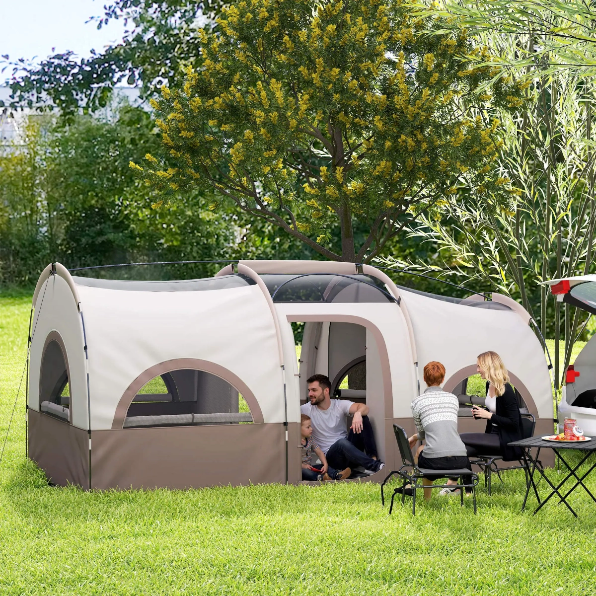 Spacious cabin-style tent in wooded area with chairs and table set outside.