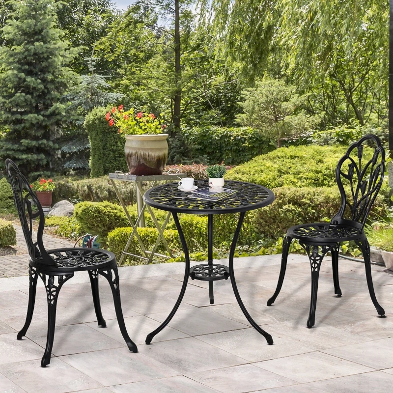 Black cast aluminum patio table and chairs on stone patio in green garden.