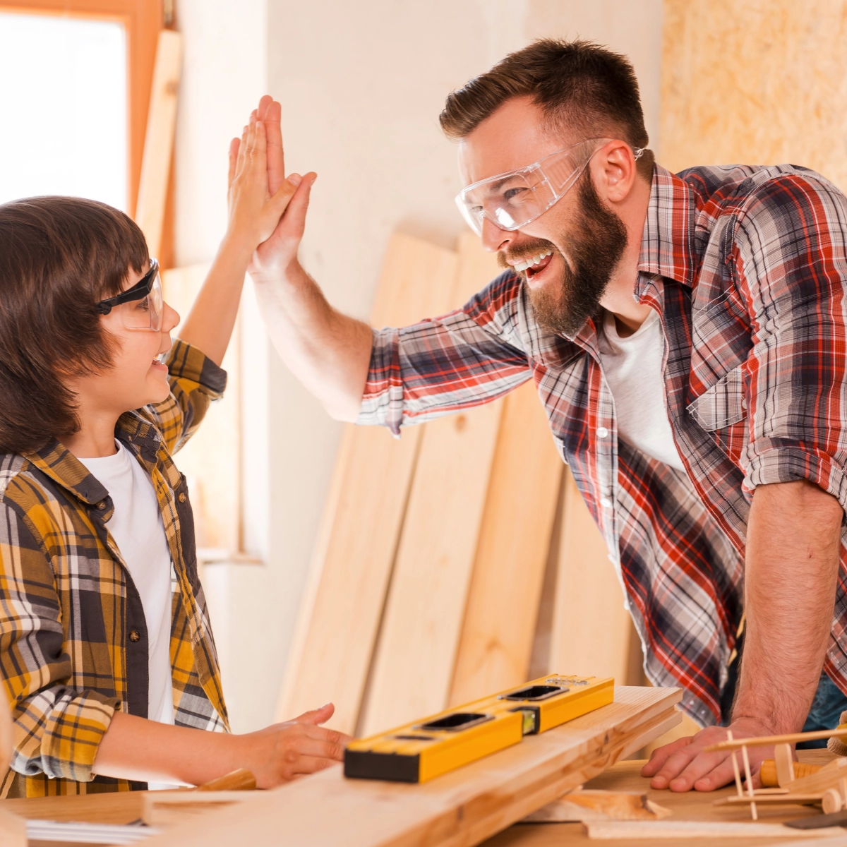 Father and son celebrating woodworking project with high-five in a workshop.