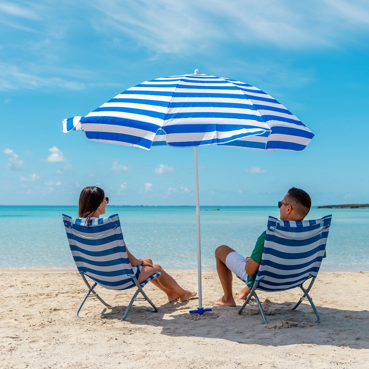 Couple relaxing under a striped beach umbrella, enjoying a tropical beach day.
