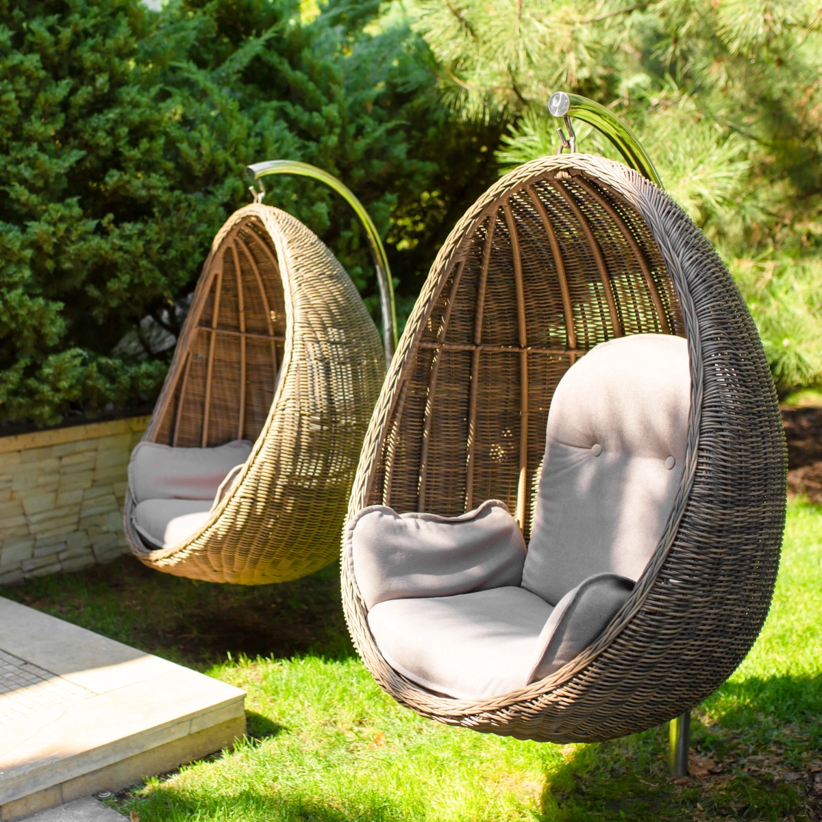 Relaxing outdoor egg chairs hanging under the shade of trees in a garden.