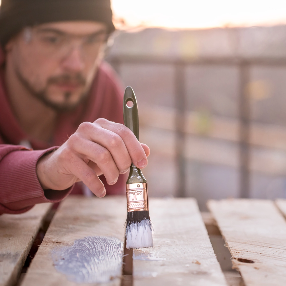 Man painting wooden pallet with brush during DIY patio furniture project.