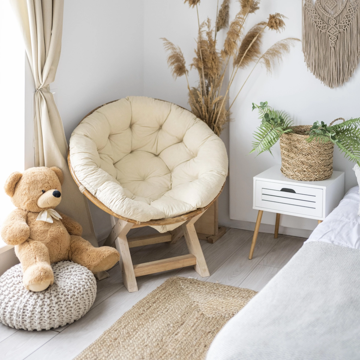 Plush papasan chair in a warm bedroom, accompanied by a teddy bear and plants.