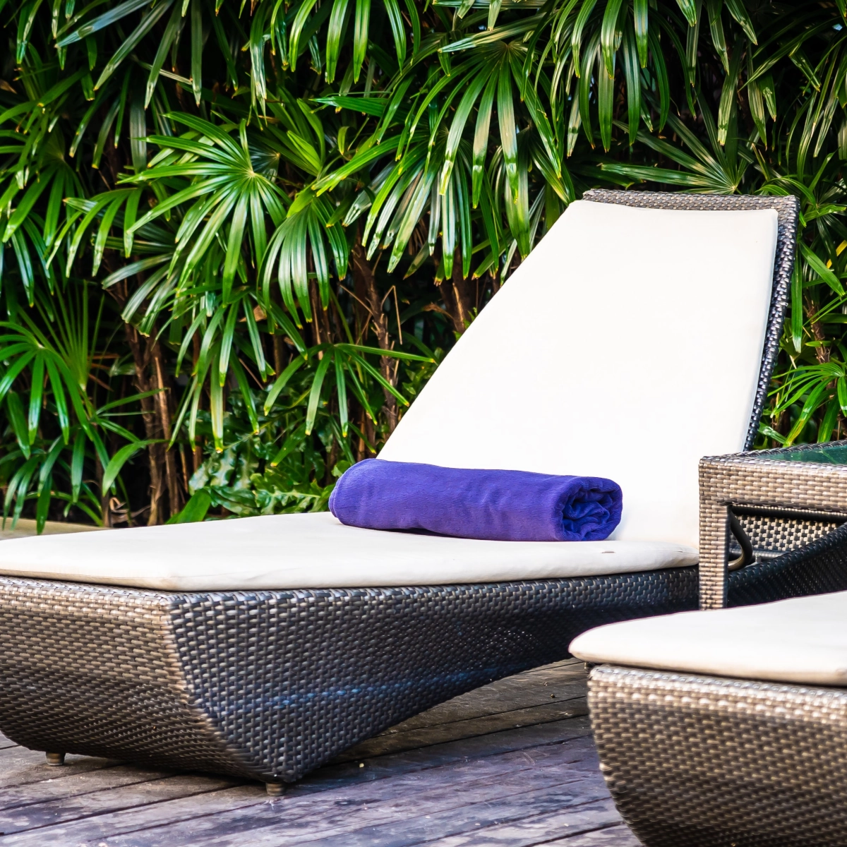 Comfortable lounge chair with purple towel in a lush garden setting for relaxation.
