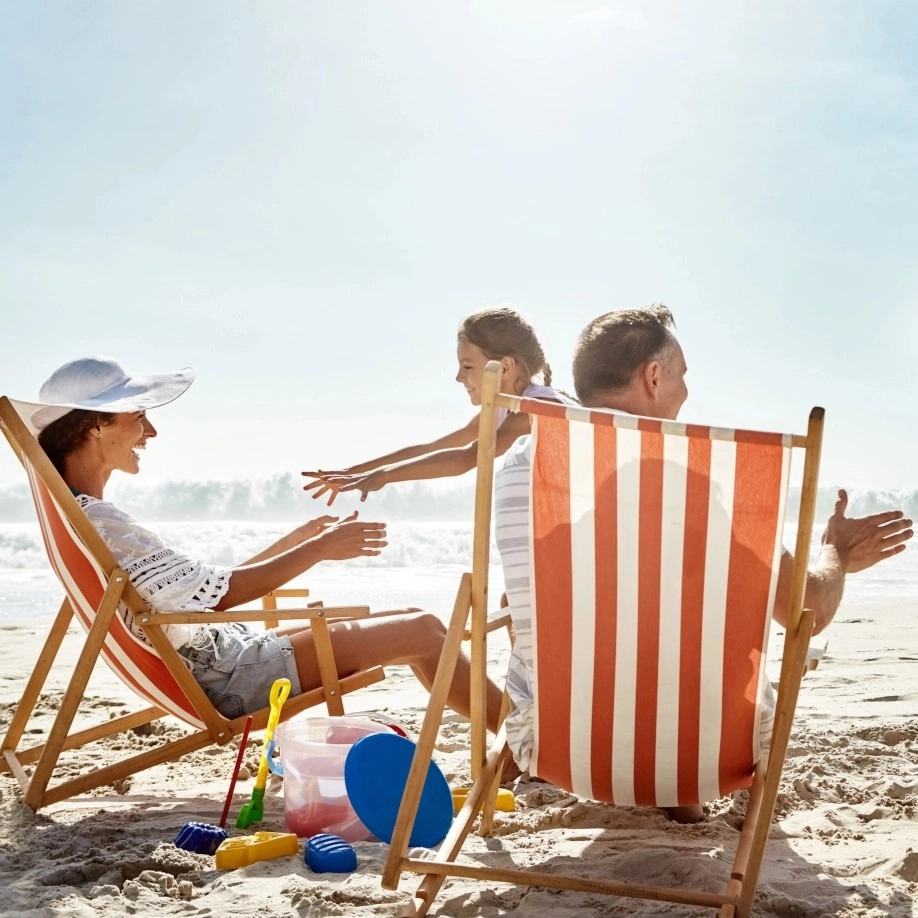 Family enjoying quality time together on striped beach chairs by the ocean.