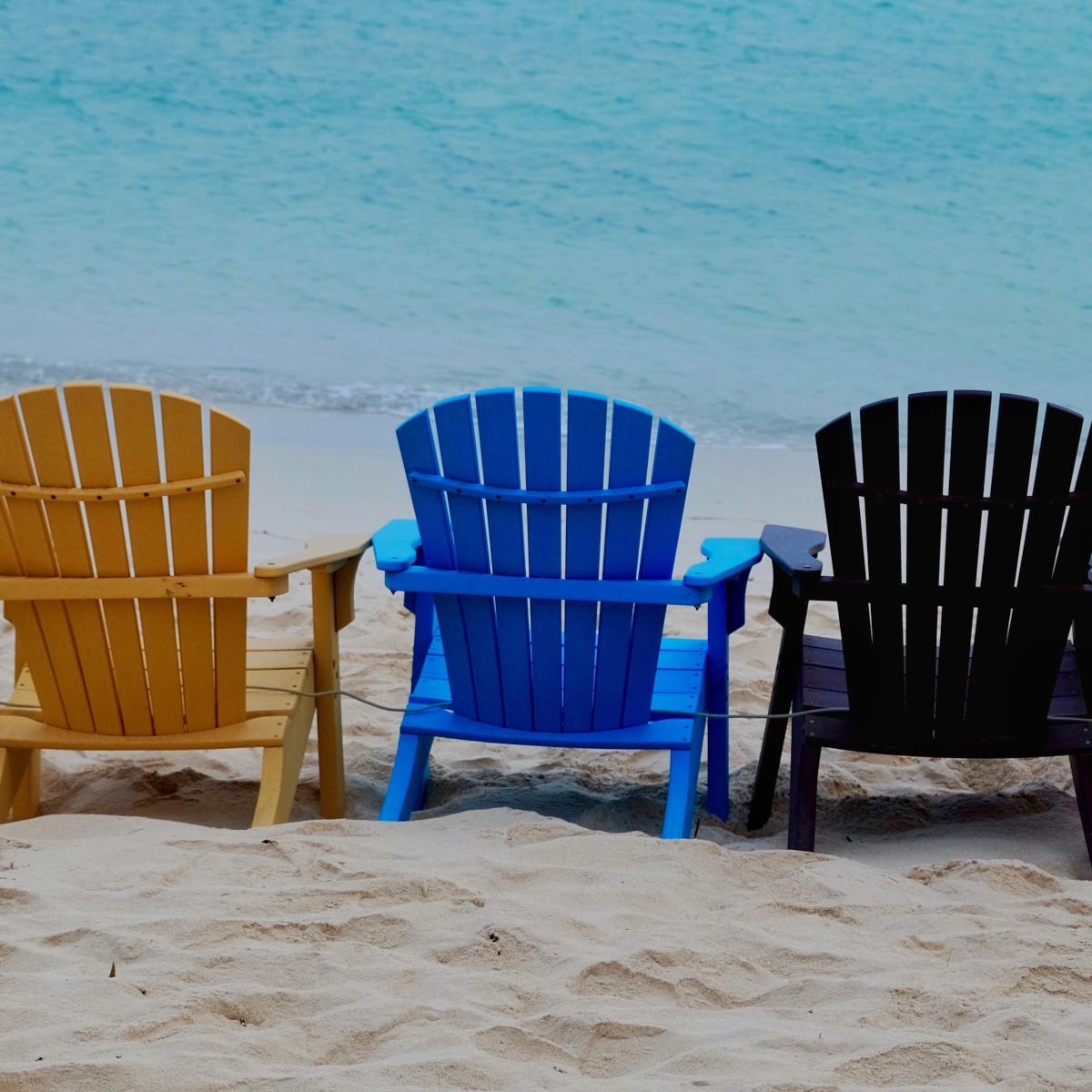 Variety of beach chairs with different designs placed on a sandy beach.