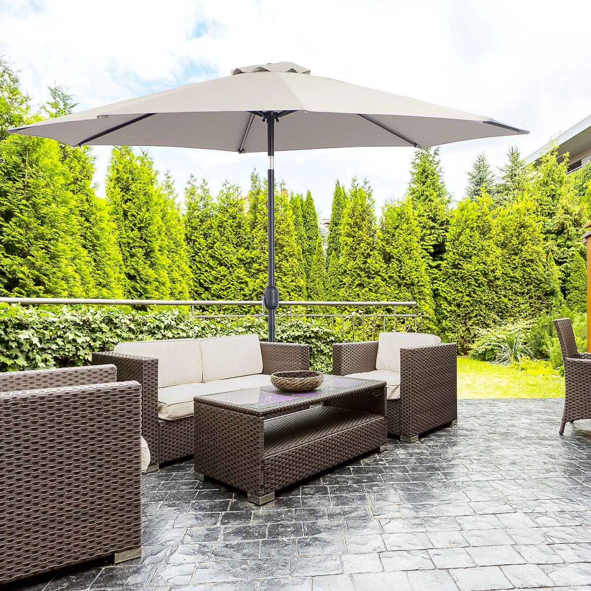 Beige outdoor umbrella shading patio furniture in a landscaped garden area.