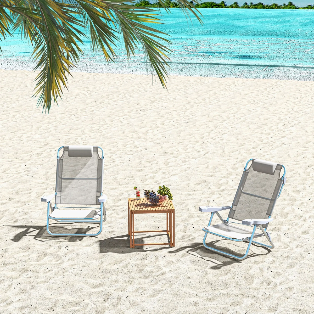 Two mesh beach chairs with headrests beside a wooden table on white sand near turquoise water.
