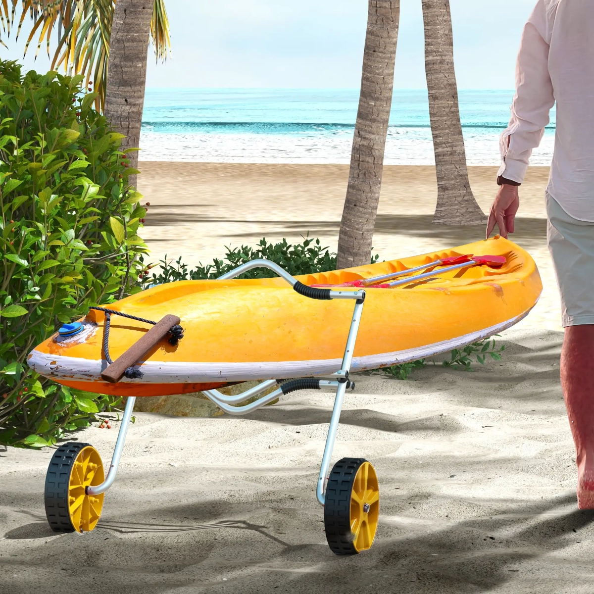 Man pulling a yellow kayak on a cart across sandy beach with palm trees.