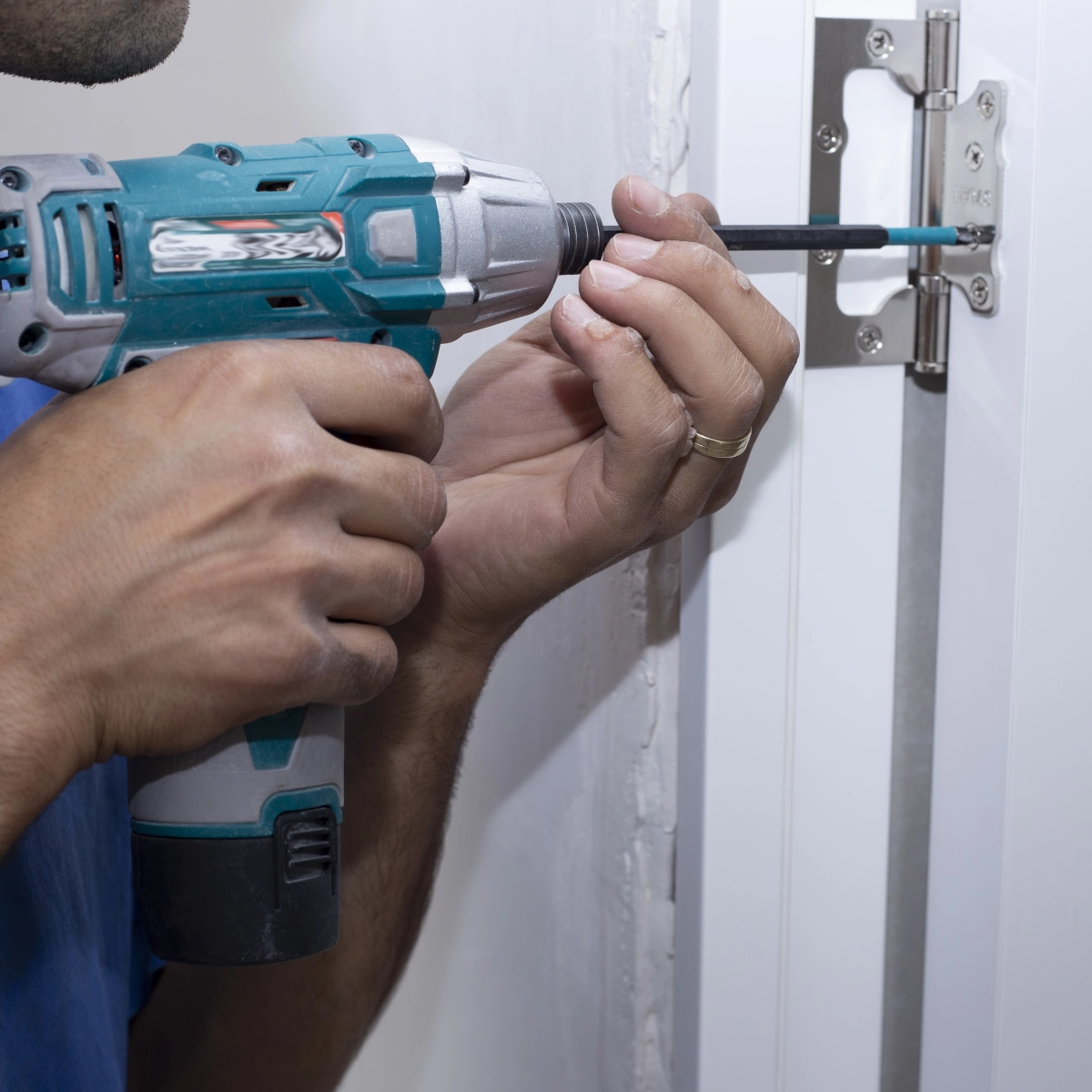 Man using a drill to adjust door hinge for wider furniture clearance.