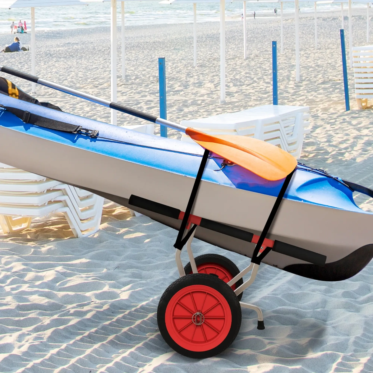 Blue kayak secured on red-wheeled cart sitting on beach sand near white sun loungers.