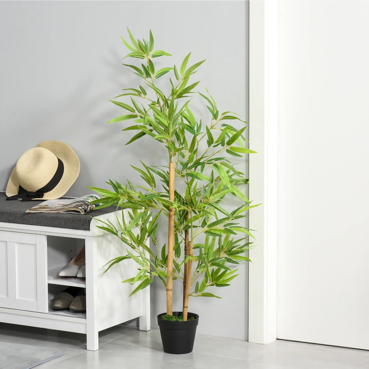 Tall artificial bamboo plant in black pot placed beside a bench in a modern entryway.