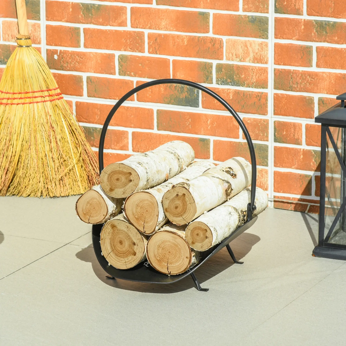 Small metal firewood basket with a curved handle holding birch logs against a brick wall.