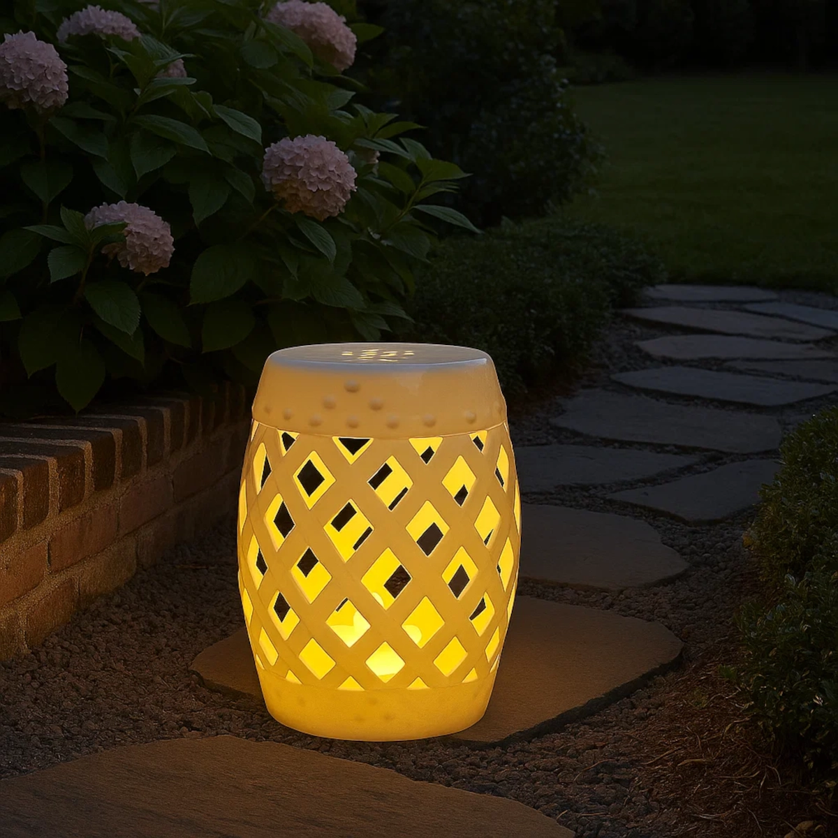 Illuminated white garden stool glowing along a garden path, surrounded by flowering hydrangea shrubs.