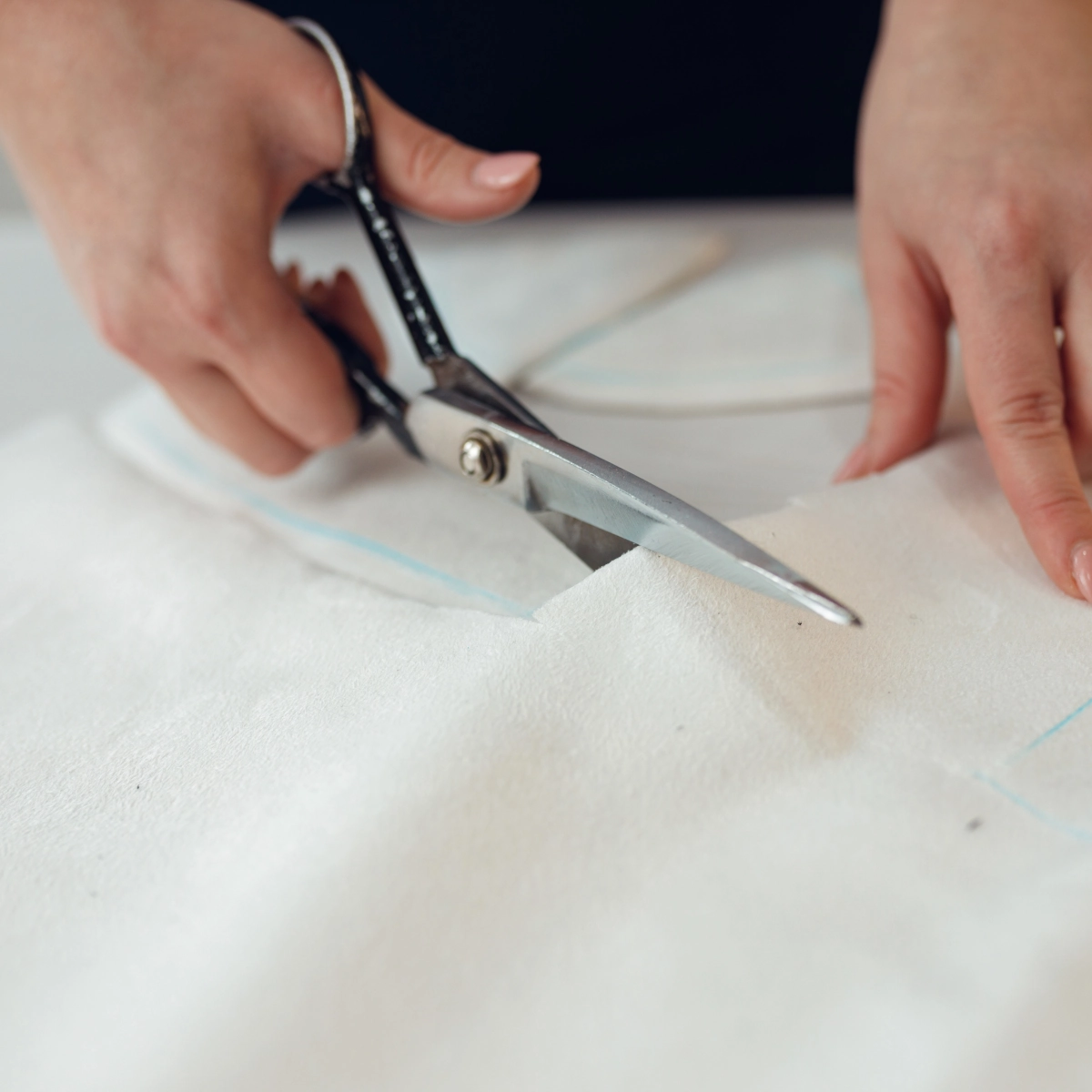 Cutting white fabric with scissors along a blue chalk line for upholstery.