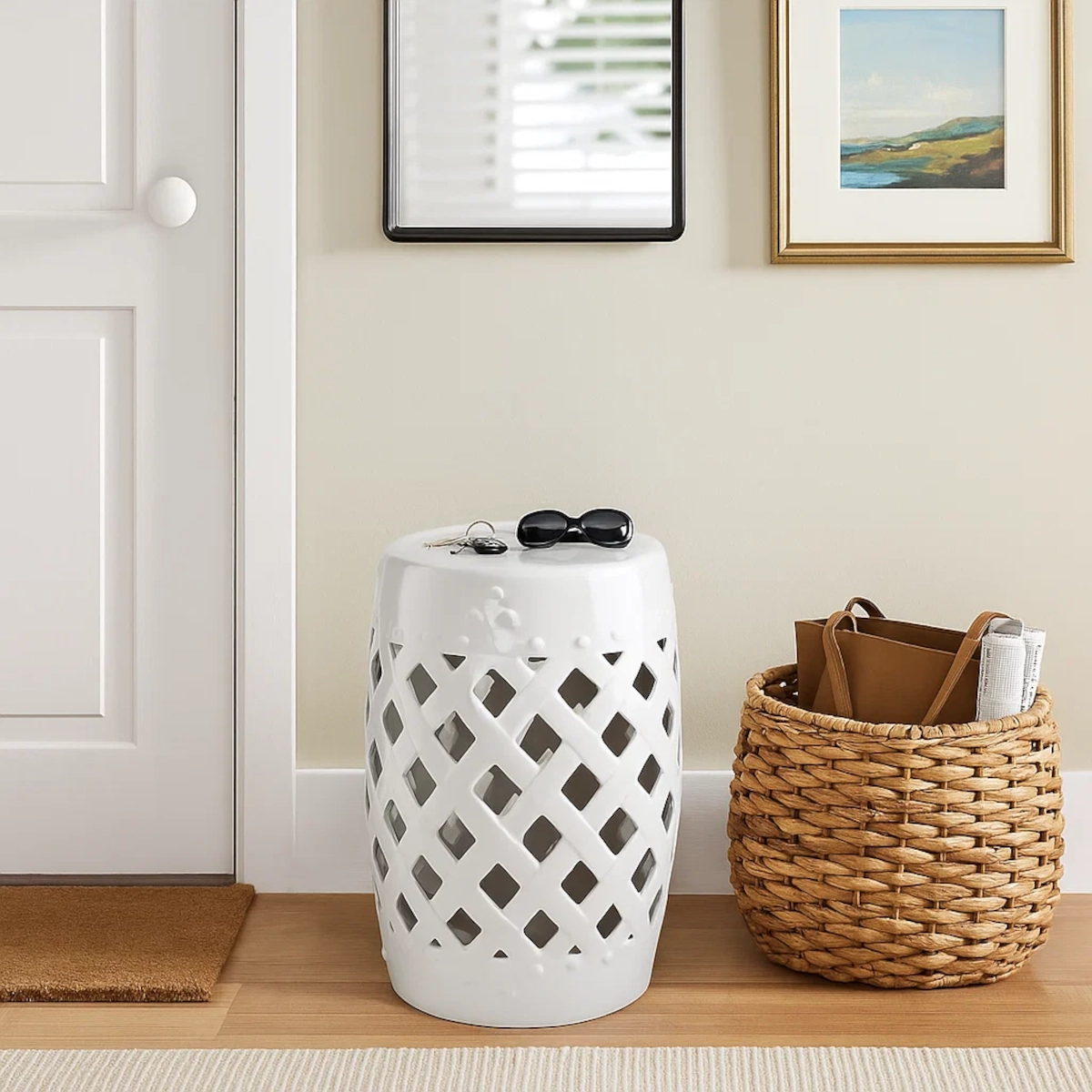 Entryway with glossy white garden stool, basket tote, sunglasses, and framed artwork on the wall.