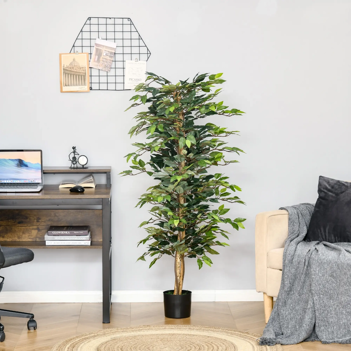 Artificial ficus tree in black pot next to home office desk and beige sofa in bright space.