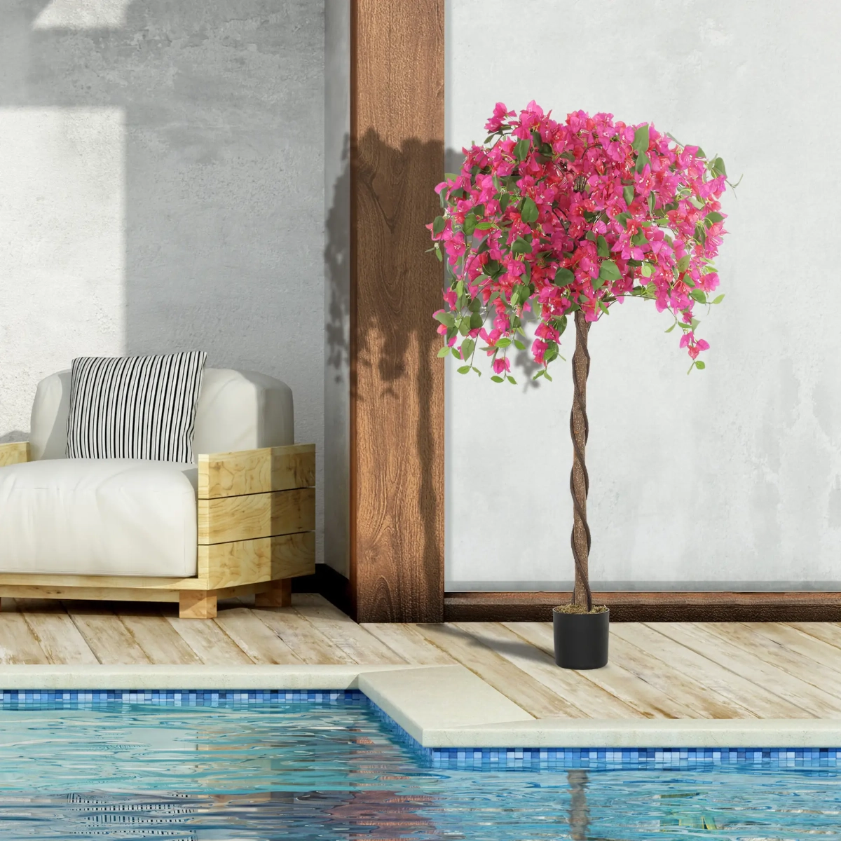 Artificial flowering tree with pink blooms in black pot by outdoor pool and modern wooden sofa.