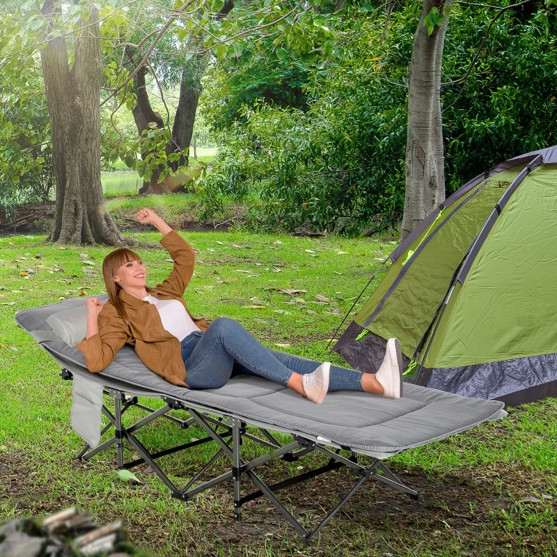 Foldable camping cot with thick mattress and attached pillow set up outdoors on grass..