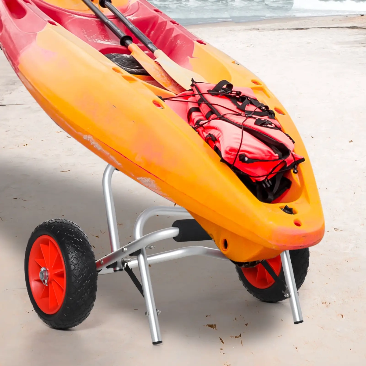 Orange kayak resting on compact folding cart with red wheels and beach background.