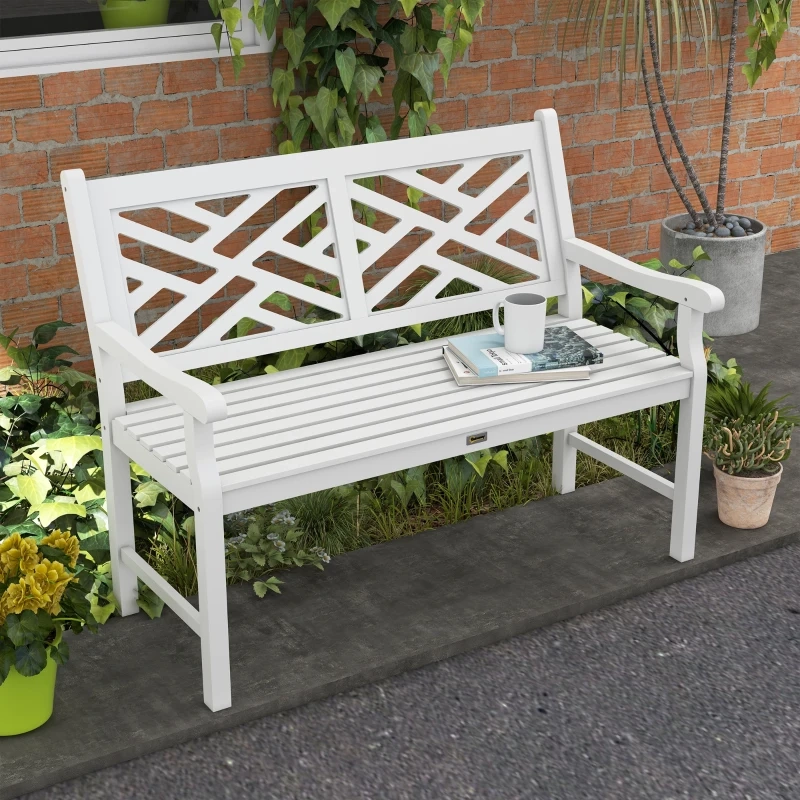 White slatted wooden garden bench surrounded by plants and placed beside a brick wall.