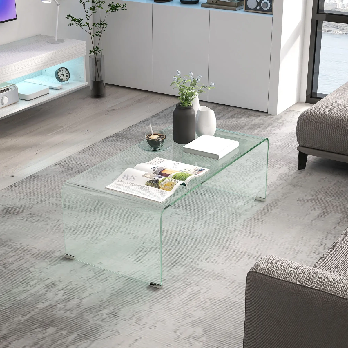 Transparent glass coffee table with curved edges placed in a minimalist modern living room.