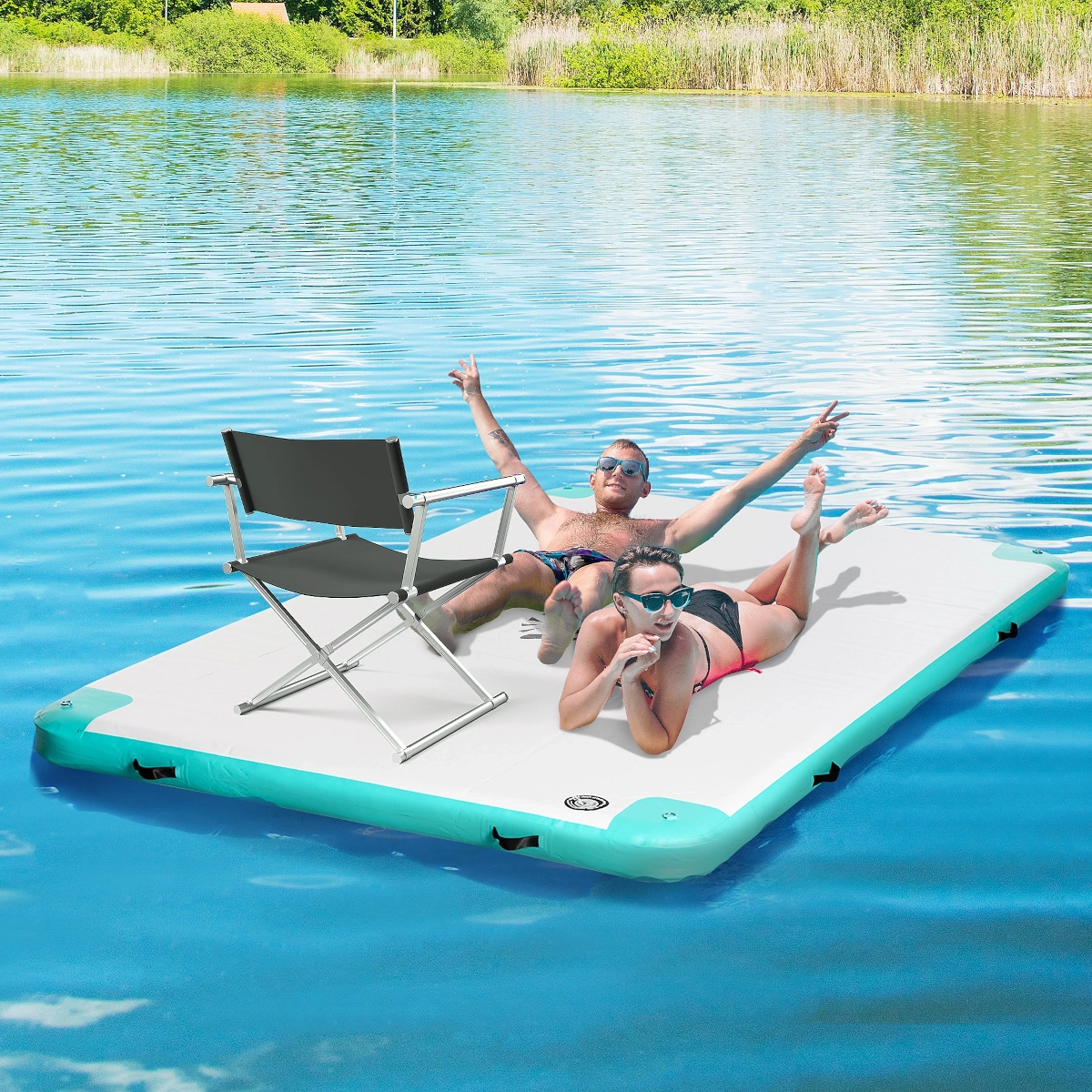 Couple relaxing on anchored floating mat in lake under sunny skies with scenic view.