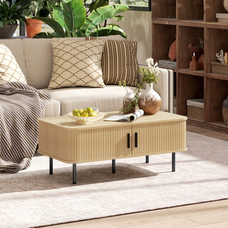Modern living room with patterned pillows, houseplants, and a light wood coffee table on a large rug.