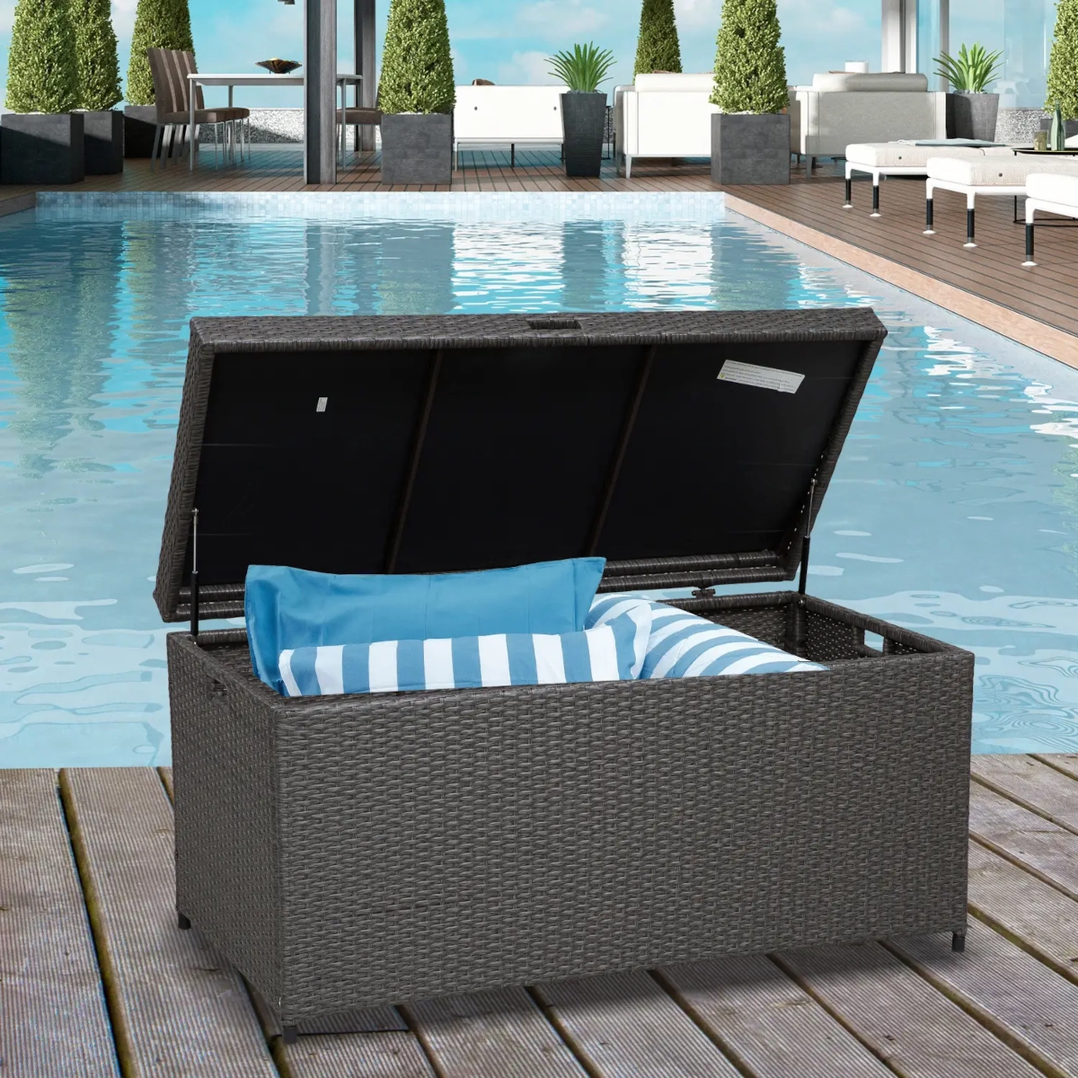 Wicker-style outdoor storage box with cushions beside pool under sunny sky.