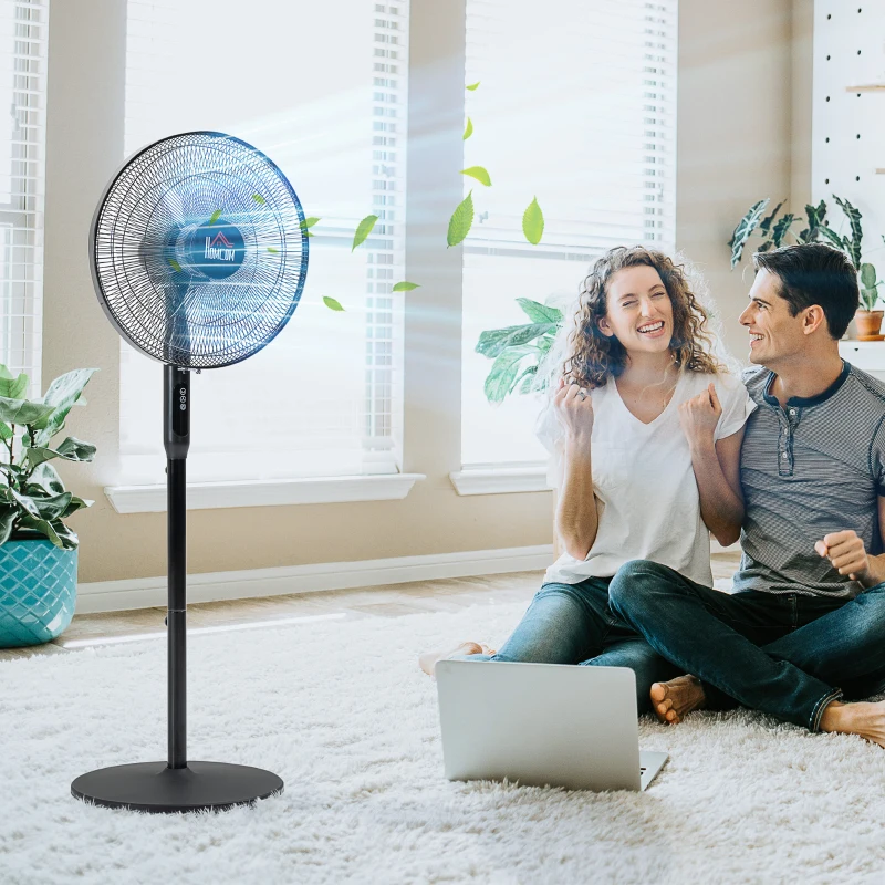 Couple enjoying clean breeze from electric stand fan indoors