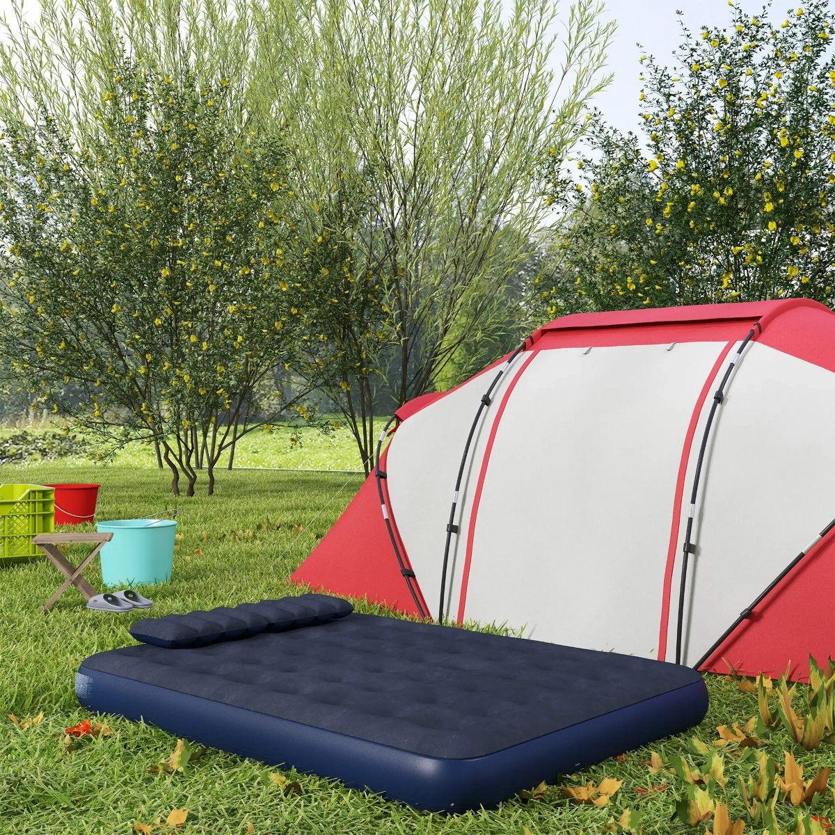 Air mattress and red tent set up on grass near trees with camping supplies.