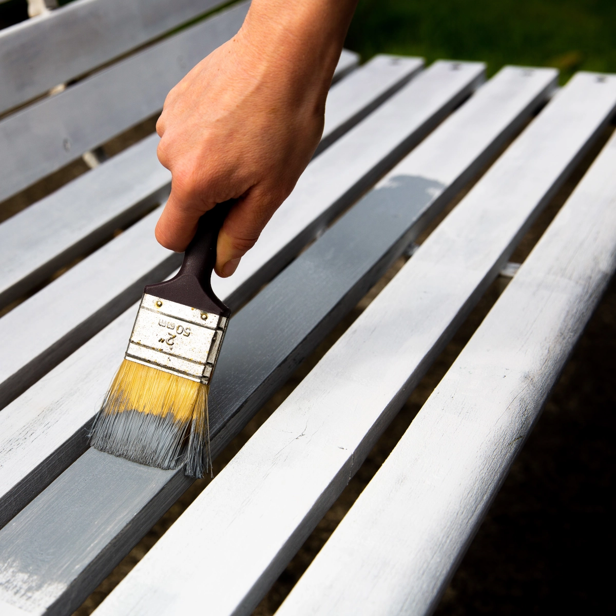 Hand painting wooden garden bench with gray primer for outdoor weather protection.