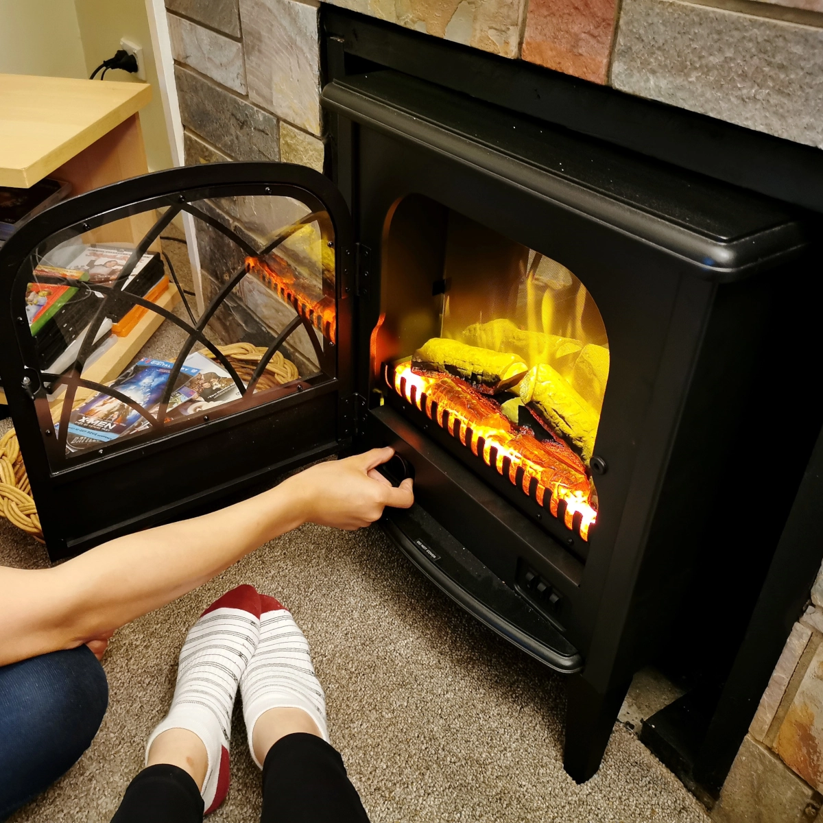 Person manually turning on an electric fireplace while sitting near glowing flame display.