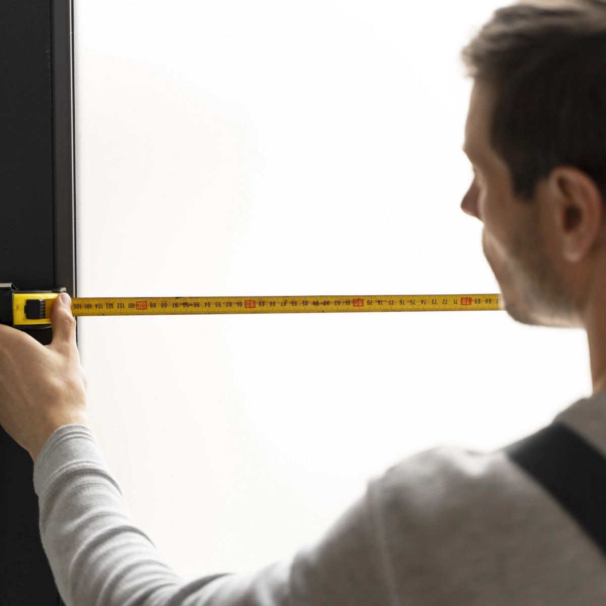 Man holding a tape measure to check width of doorway for furniture fitting.