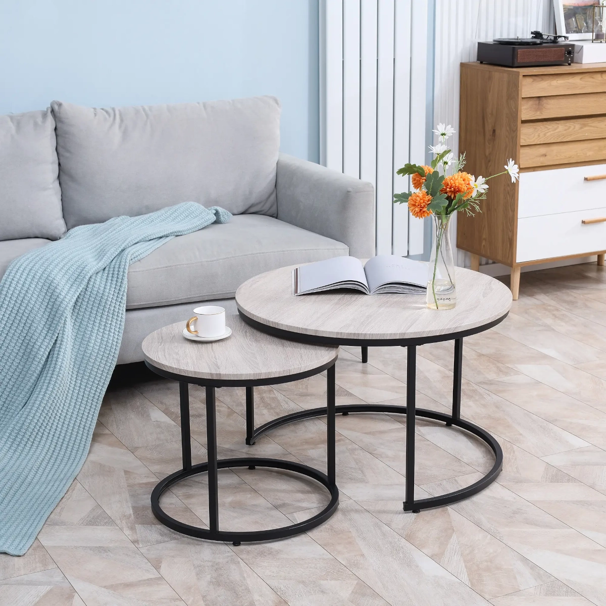 Two-tone round nesting tables beside a grey couch with flowers and a coffee cup on top.