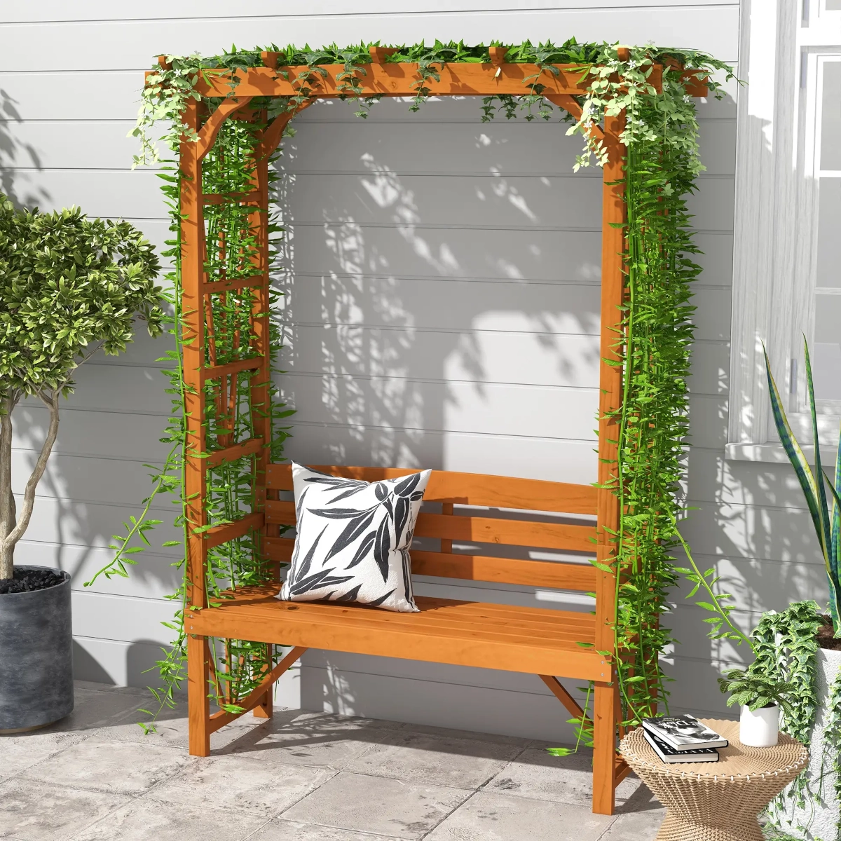 Wooden garden bench with trellis arbor covered in green vines on a tiled patio.