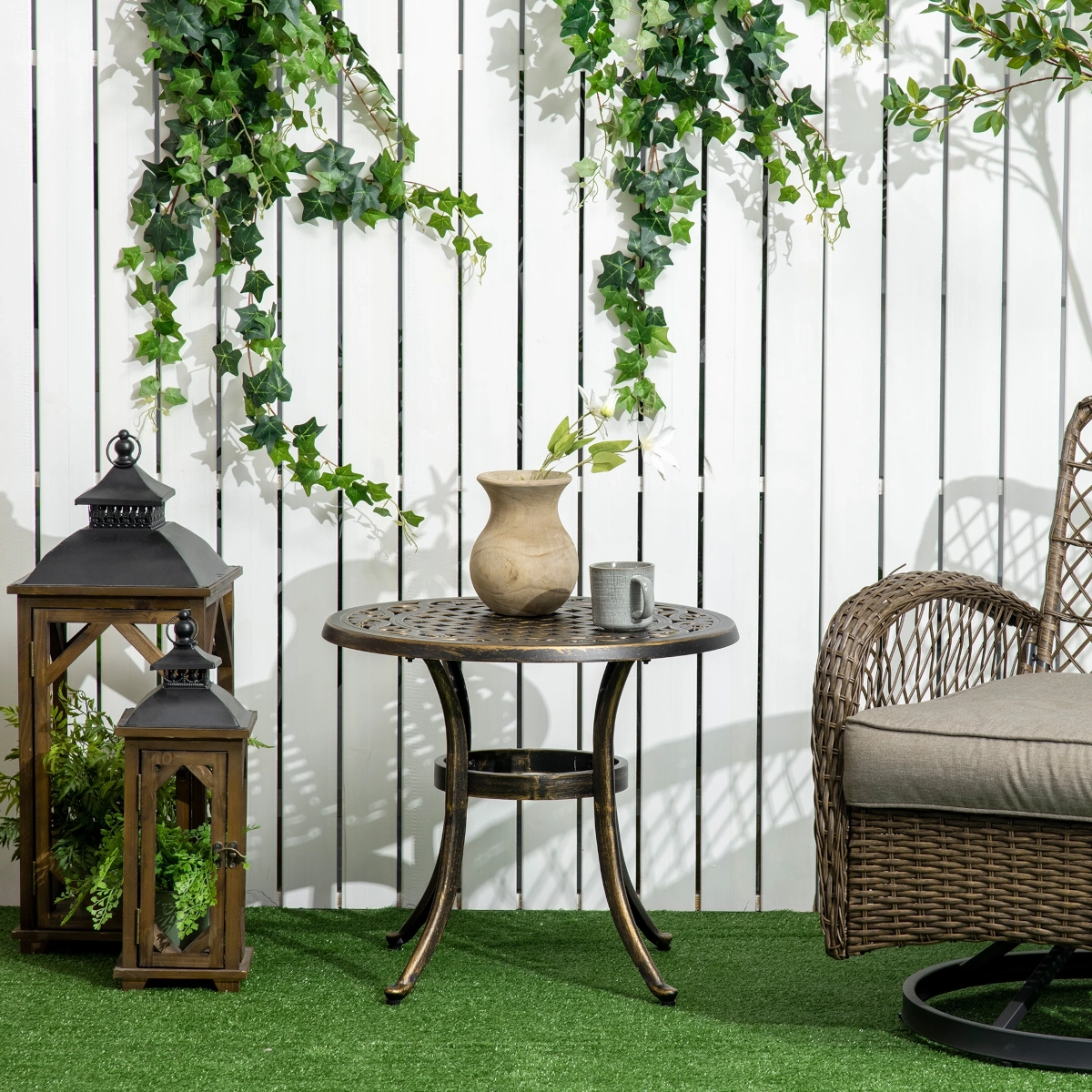 Outdoor patio setup with metal table, wicker chair, hanging ivy, lanterns, and white slat fence.