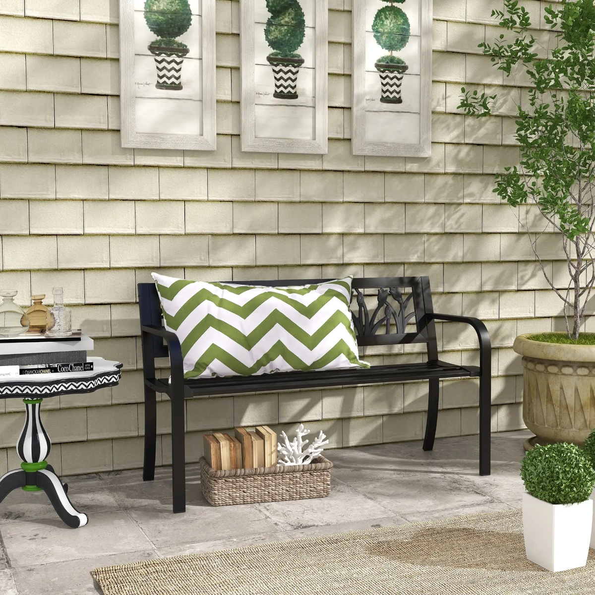 Black metal bench with decorative backrest and green chevron pillow on a stone patio.