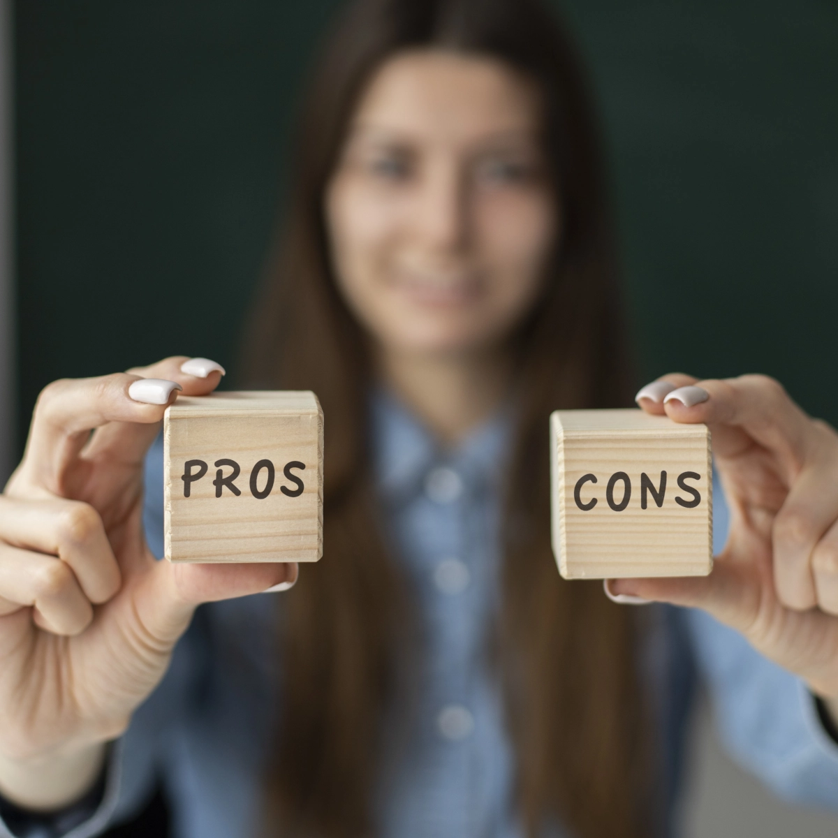 Closeup of a woman holding wooden blocks labeled pros and cons in both hands.