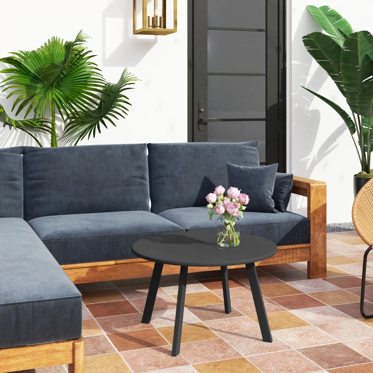 Black round coffee table with vase of pink roses in a patio lounge setup with blue cushions.