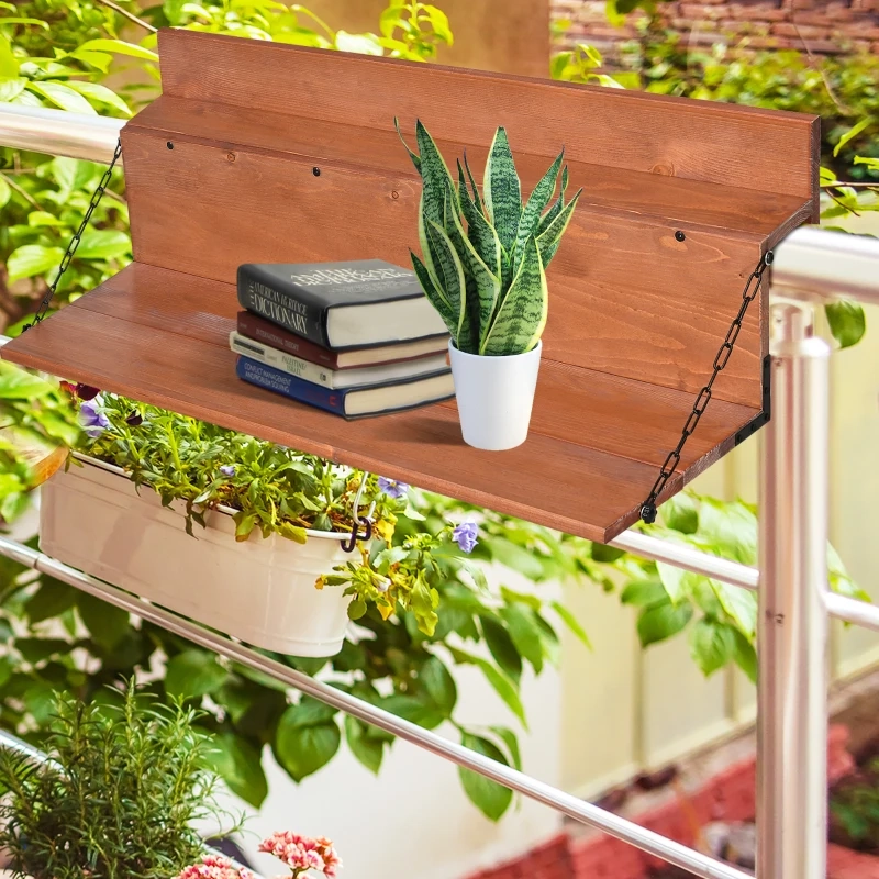 Wooden folding table on balcony railing with books and a potted plant, surrounded by green foliage.