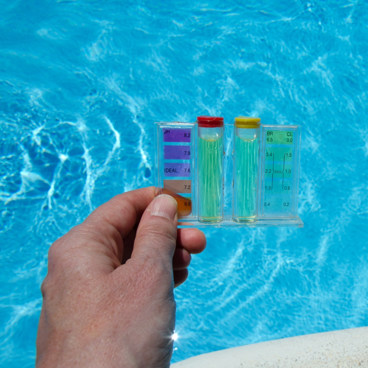 Hand using water test kit to check and adjust chemical balance in pool water.