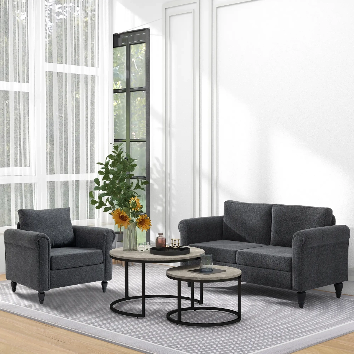 Dark grey armchair and loveseat paired with round nesting tables in a bright, elegant space.