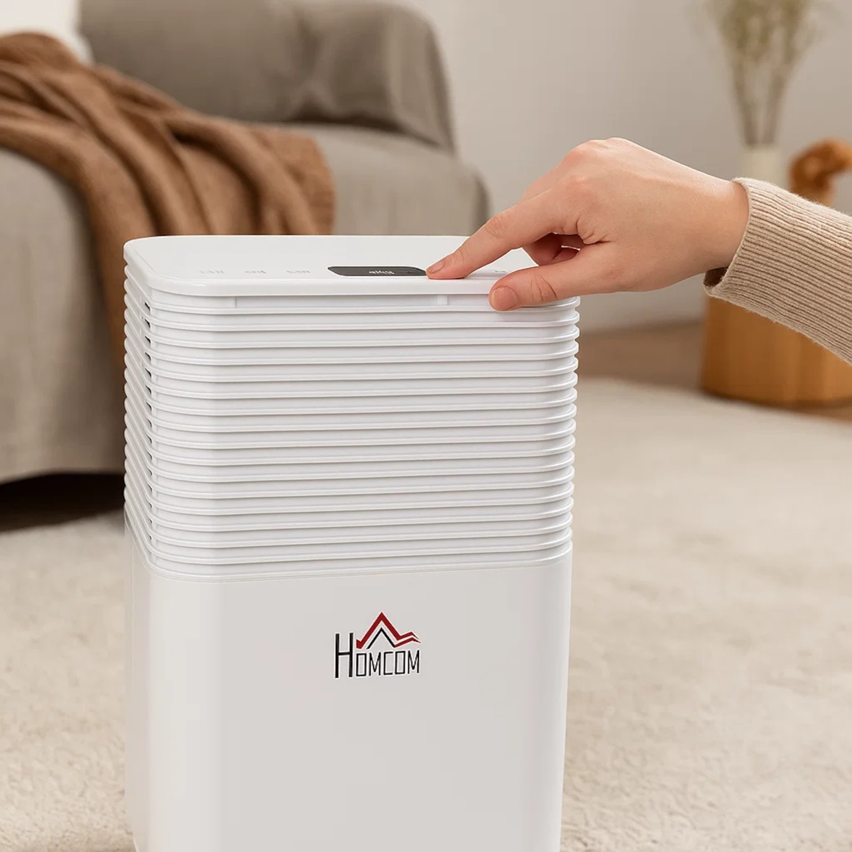 Hand pressing control panel button on white HOMCOM dehumidifier in a carpeted living room.