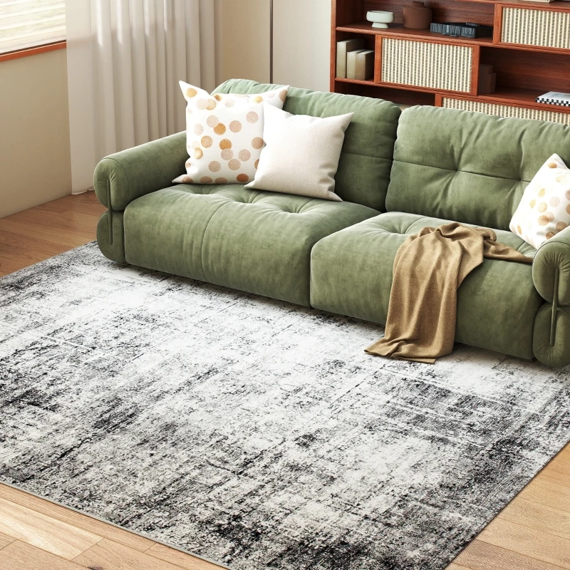 Green velvet sofa on a textured grey-black area rug with bookshelf and natural lighting in the background.