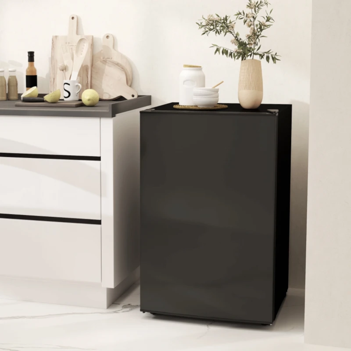 Matte black mini fridge placed beside kitchen counter with decor items on top