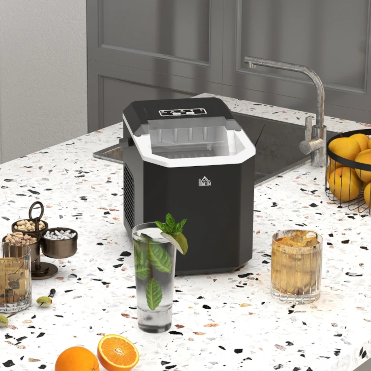 Portable ice maker on kitchen counter beside drinks and citrus, ready for cleaning or use.