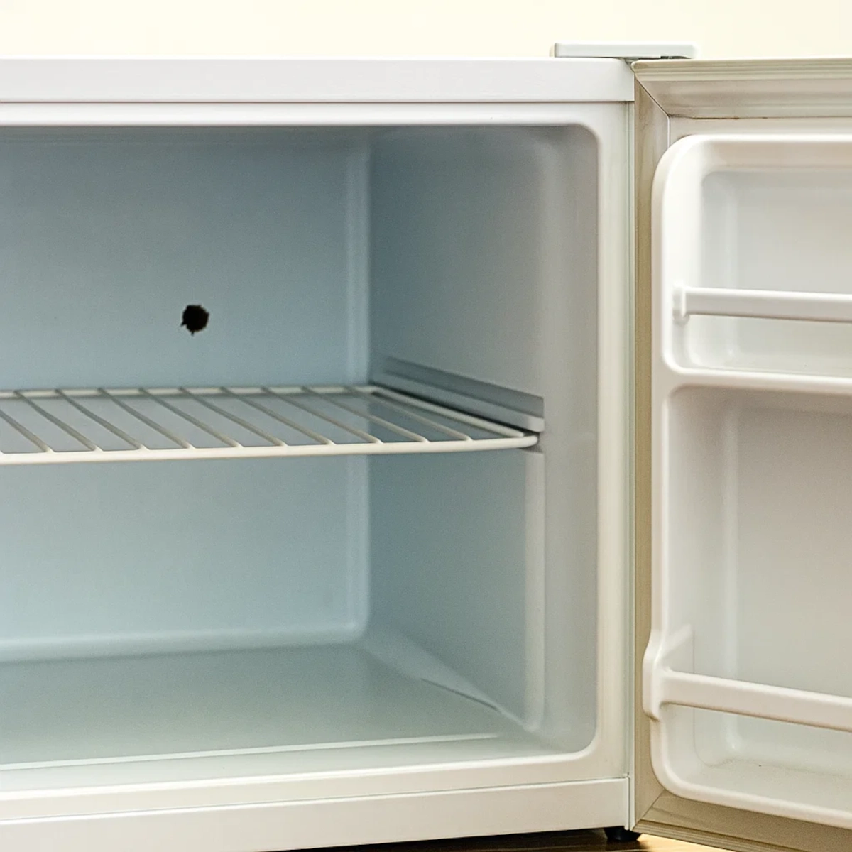 Mini fridge interior showing punctured hole in freezer wall.